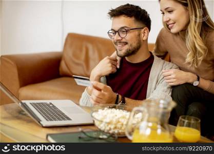 Young woman and young man using laptopfor online payment while sitting by the sofa at home