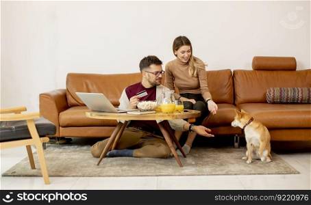Young woman and young man using laptopfor online payment while sitting by the sofa with their shiba inu dog at home
