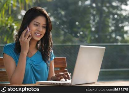 Young woman answering phone call while working on laptop