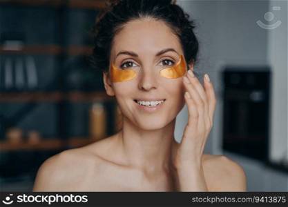 Young woman applies collagen eye patches, happy European girl in spa mode. Golden anti-wrinkle patches enhance skincare routine.