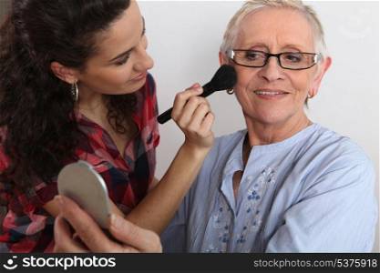 Young woman applying blush on her grandmother&rsquo;s cheeks