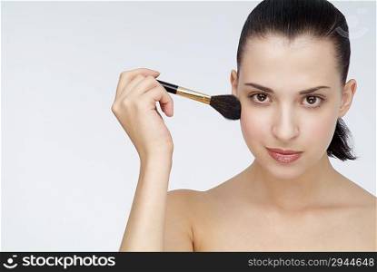 Young woman applying blush to her cheek