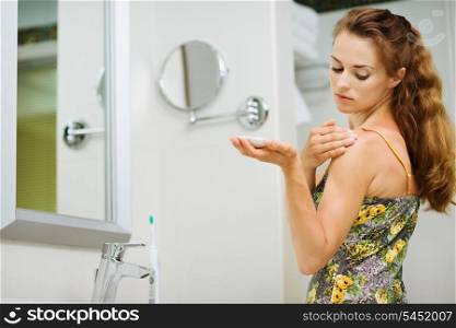 Young woman applying body creme on shoulder in bathroom