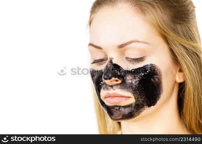 Young woman applying carbo detox black mask to her face. Teen girl taking care of oily skin, cleaning the pores. Spa treatment. Skincare.. Woman applying black cleanser mask to face
