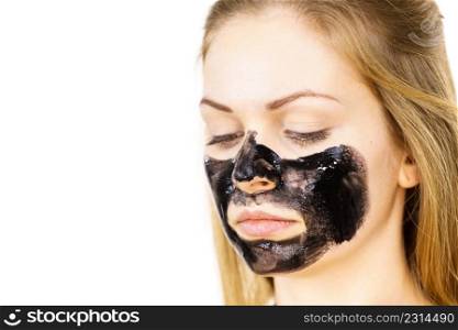 Young woman applying carbo detox black mask to her face. Teen girl taking care of oily skin, cleaning the pores. Spa treatment. Skincare.. Woman applying black cleanser mask to face
