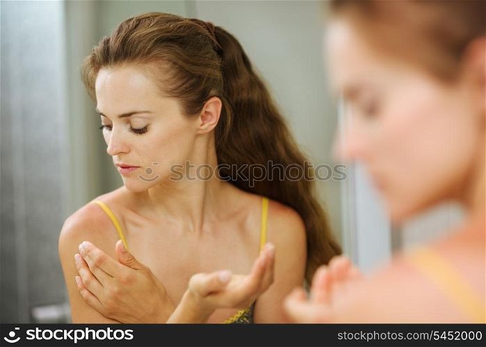 Young woman applying creme on shoulder in bathroom