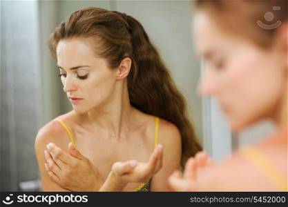 Young woman applying creme on shoulder in bathroom