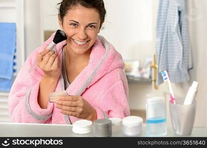 Young woman applying face powder with brush in the bathroom