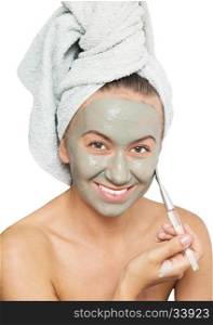 Young woman applying facial clay mask to her face using brush