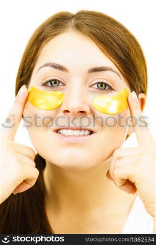 Young woman applying golden collagen patches under eyes. Mask removing wrinkles and dark circles. Girl taking care of delicate skin around eye. Beauty treatment.. Woman with gold patches under eyes