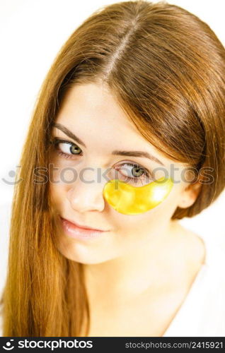 Young woman applying golden collagen patches under eyes. Mask removing wrinkles and dark circles. Girl taking care of delicate skin around eye. Beauty treatment.. Woman with gold patches under eyes