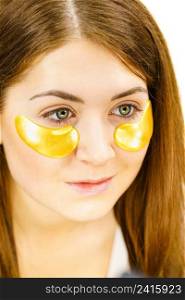 Young woman applying golden collagen patches under eyes. Mask removing wrinkles and dark circles. Girl taking care of delicate skin around eye. Beauty treatment.. Woman with gold patches under eyes