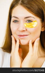 Young woman applying golden collagen patches under eyes. Mask removing wrinkles and dark circles. Girl taking care of delicate skin around eye. Beauty treatment.. Woman with gold patches under eyes