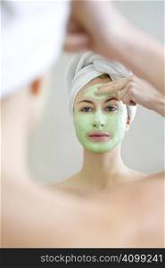 Young woman applying green algae facial mask.