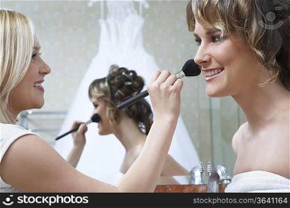 Young woman applying make-up to bride&acute;s face