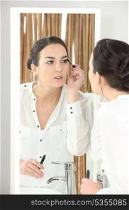 Young woman applying mascara in front of a bathroom mirror