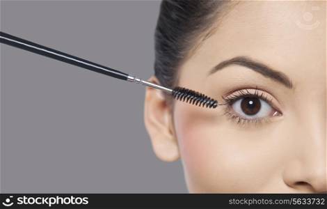 Young woman applying mascara over grey background