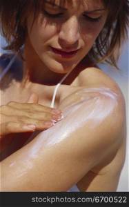 Young woman applying suntan lotion