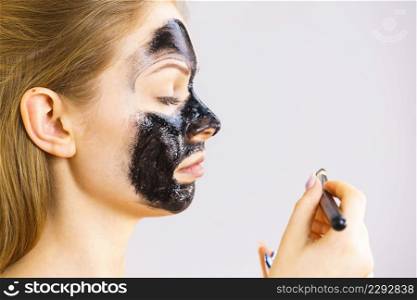 Young woman applying with brush black detox mud mask to her face. Girl taking care of skin. Spa treatment. Skincare. Side view. Woman applying black mask to skin face