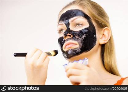 Young woman applying with brush black detox mud mask to her face. Girl taking care of skin. Beauty treatment. Skincare.. Woman applying black mud mask to face