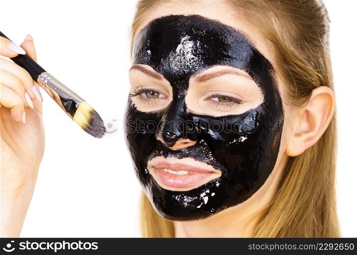 Young woman applying with brush black detox peel off mask to her face. Girl taking care of skin. Beauty treatment. Skincare.. Woman applying black mud mask to face