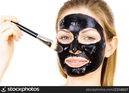 Young woman applying with brush black detox peel off mask to her face. Girl taking care of skin. Beauty treatment. Skincare.. Woman applying black mud mask to face