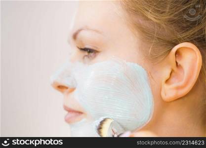 Young woman applying with brush green white mud mask to her face. Teen girl taking care of oily skin, purifying the pores. Beauty treatment. Skincare.. Girl apply green mud mask to face