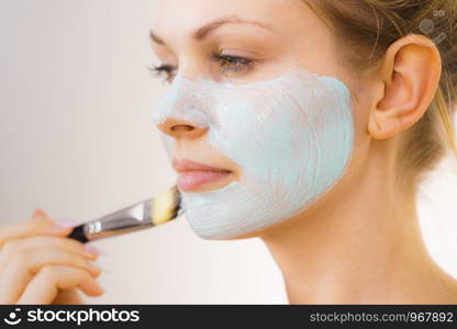 Young woman applying with brush green white mud mask to her face. Teen girl taking care of oily skin, purifying the pores. Beauty treatment. Skincare.. Girl apply green mud mask to face