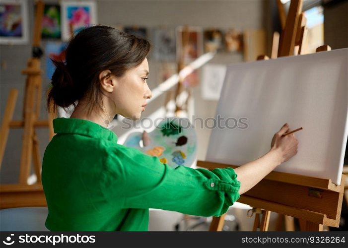 Young woman artist starting to draw on blank empty canvas with oil paints and brush in art studio workshop. Young woman starting to draw on blank empty canvas with oil paints in art studio