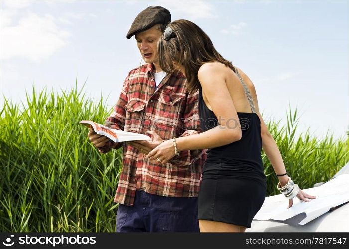 Young woman asking a farmer for information using a guide book and leaning on a map on the hood of her car