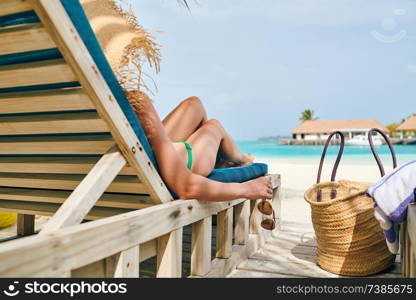 Young woman at beach on wooden sun bed loungers. Summer vacation at Maldives.