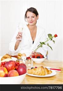 Young woman at breakfast holding a glass of champagne and a red rose for her valentine