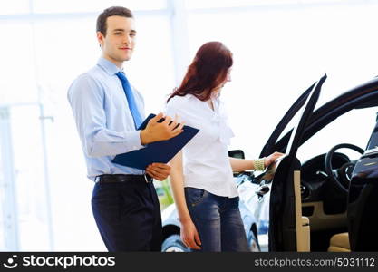 Young woman at car salon. Attractive woman at car salon with consultant choosing a car