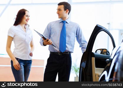 Young woman at car salon. Attractive woman at car salon with consultant choosing a car