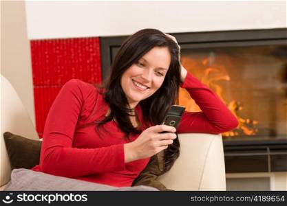Young woman at fireplace lying on sofa with mobile phone