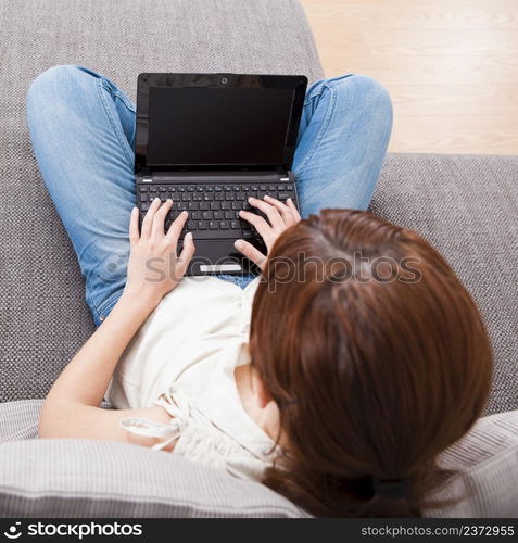 Young woman at home seated on sofa and working with a laptop