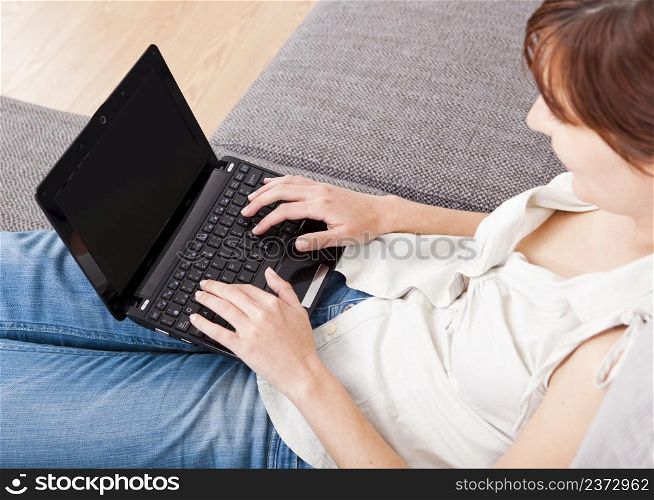 Young woman at home seated on sofa and working with a laptop