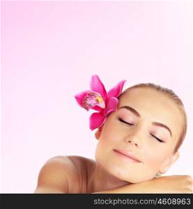 Young woman at spa salon, beautiful girl sleeping on massage table, pretty female with pink orchid in her hair, attractive lady relaxed, beauty and health care concept, close up portrait of cute model