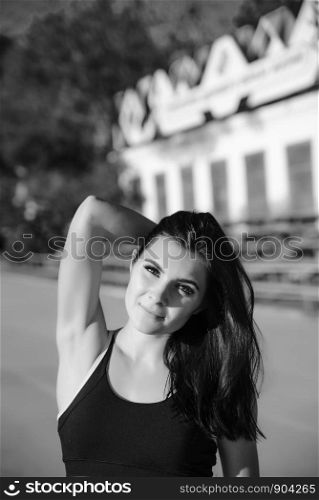 Young woman athlete on stadium sporty lifestyle standing on track posing looking camera smiling joyful. Portrait beautiful woman with a perfect figure in blue shorts and black top posing for the camera on running track at the stadium