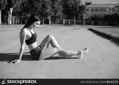 Young woman athlete on stadium sporty lifestyle standing on track posing looking camera smiling joyful. Portrait beautiful woman with a perfect figure in blue shorts and black top posing for the camera on running track at the stadium