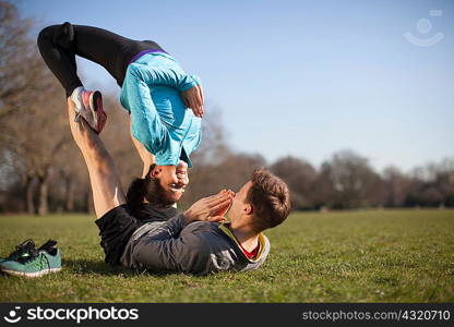 Young woman balancing on top of man practicing yoga pose in park