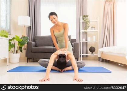 Young woman beginning yoga practice with private teacher at home. Professional instructor teaches student to do Baddha Konasana exercise or Butterfly pose, body leaning forwards over the clasped feet. Healthy lifestyle concept