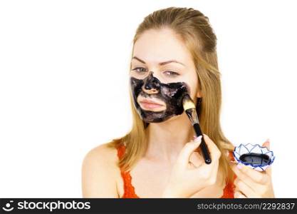 Young woman being apply with brush black detox mud mask to her face. Girl taking care of skin. Beauty treatment. Skincare.. Woman being apply black mask to skin face