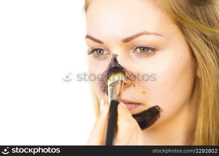 Young woman being apply with brush purifying charcoal mask, black cosmetic to her face. Female taking care of oily skin. Beauty treatment. Skincare.. Girl being apply carbo mask to skin face