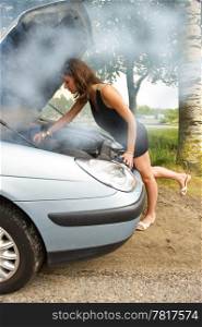 Young woman bending over the blown engine of her car, looking at the oil, whilst smoke is coming from under the hood
