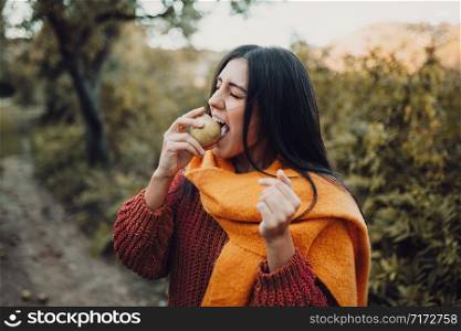 Young woman biting a pear in the field wearing a sweater
