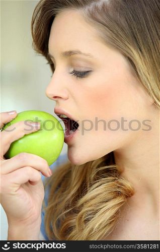 Young woman biting into a green apple