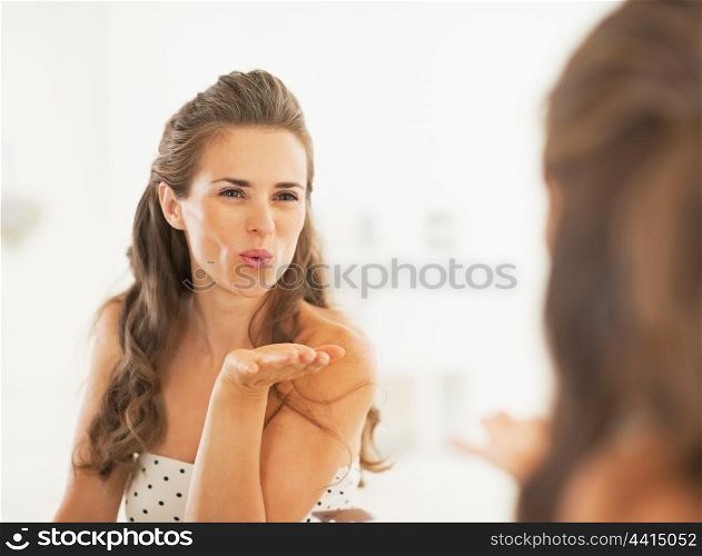 Young woman blowing air kiss in mirror