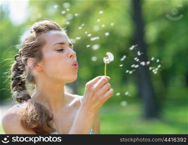 Young woman blowing away dandelion