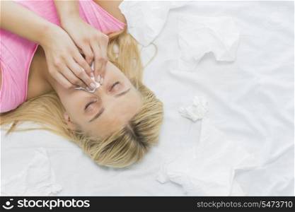 Young woman blowing nose in tissue paper while lying on bed